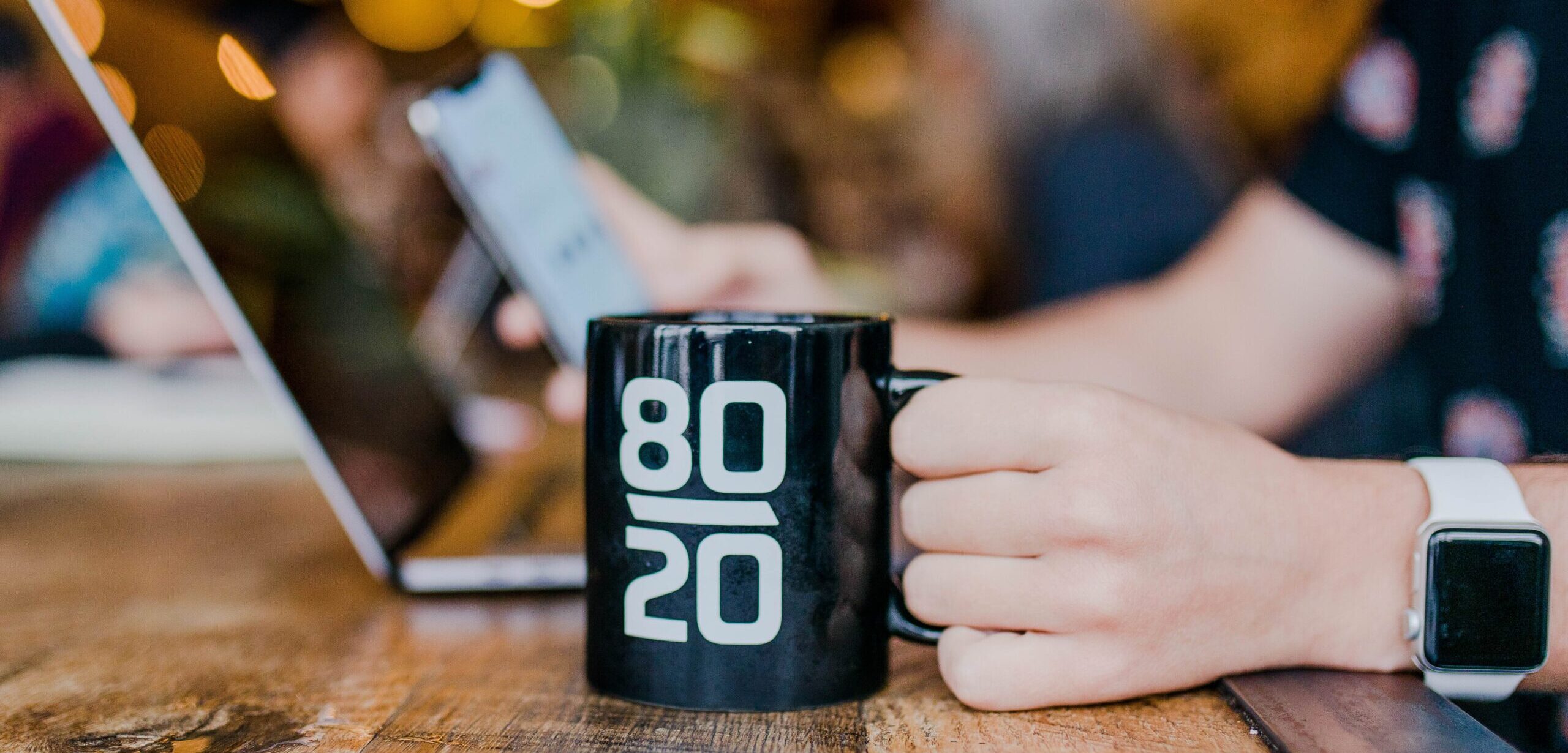 80/20 Rule for Technology Man holds coffee mug and works on phone and laptop
